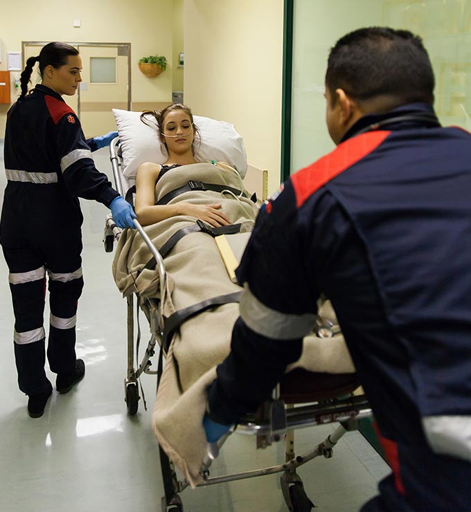two-paremedics-taking-woman-on-gurney-through-hospital